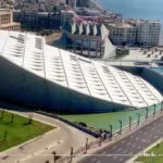 An aerial view of the Bibliotheca Alexandrina, a modern library complex in Alexandria, Egypt. The library has a distinctive disc-shaped roof, which is made up of aluminum panels that can open and close to regulate the temperature inside the building.