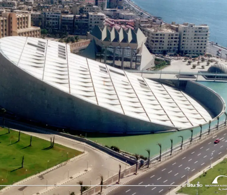 An aerial view of the Bibliotheca Alexandrina, a modern library complex in Alexandria, Egypt. The library has a distinctive disc-shaped roof, which is made up of aluminum panels that can open and close to regulate the temperature inside the building.