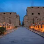 This image might depict the Karnak Temple Complex located in Luxor, Egypt. The complex is a vast collection of temples, pylons, and other structures, and is one of the largest religious sites in the world. The statue in the foreground may be a sphinx, a mythical creature with the body of a lion and the head of a human or animal.