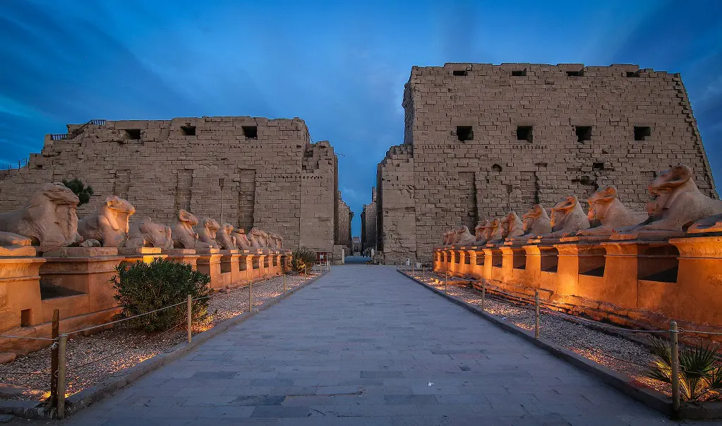 This image might depict the Karnak Temple Complex located in Luxor, Egypt. The complex is a vast collection of temples, pylons, and other structures, and is one of the largest religious sites in the world. The statue in the foreground may be a sphinx, a mythical creature with the body of a lion and the head of a human or animal.